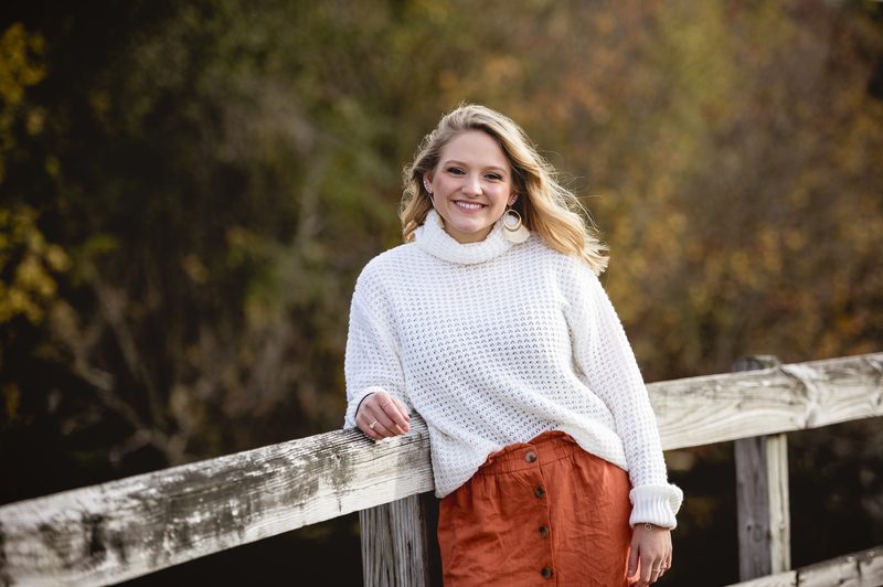 Fall senior photo ideas - Shallow focus shot of a female leaning against a wooden fence and smiling at the camera