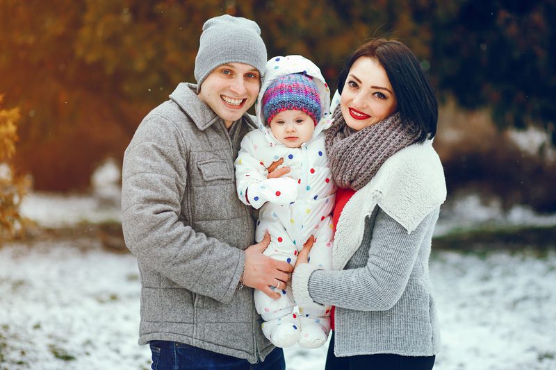 A young cheerful family in winter clothes walks in a snowy park