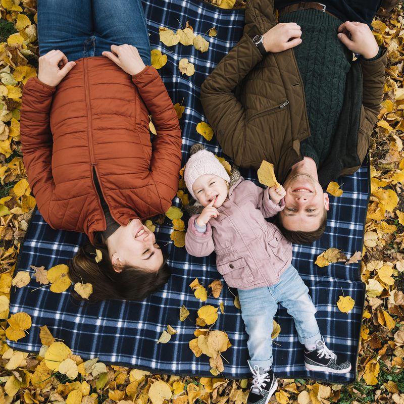 parents-with-daughter-lying-autumn-leaves-park-Fall-Family-Photography-Ideas