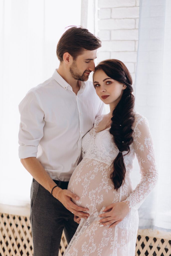 Tender hugs of young expecting couple standing in bright studio