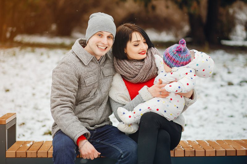 A young cheerful family in winter clothes sitting in a snowy park