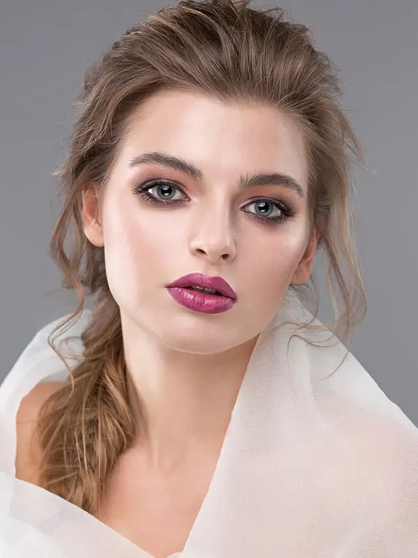 Close-up portrait of a woman with blue eyes, pink lipstick, natural makeup, and sheer white fabric.