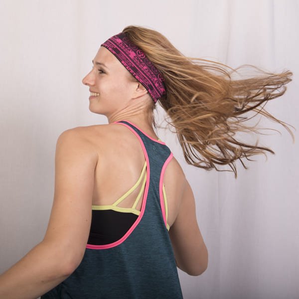 Woman with long hair in blue tank top and pink headband turns smiling against plain background
