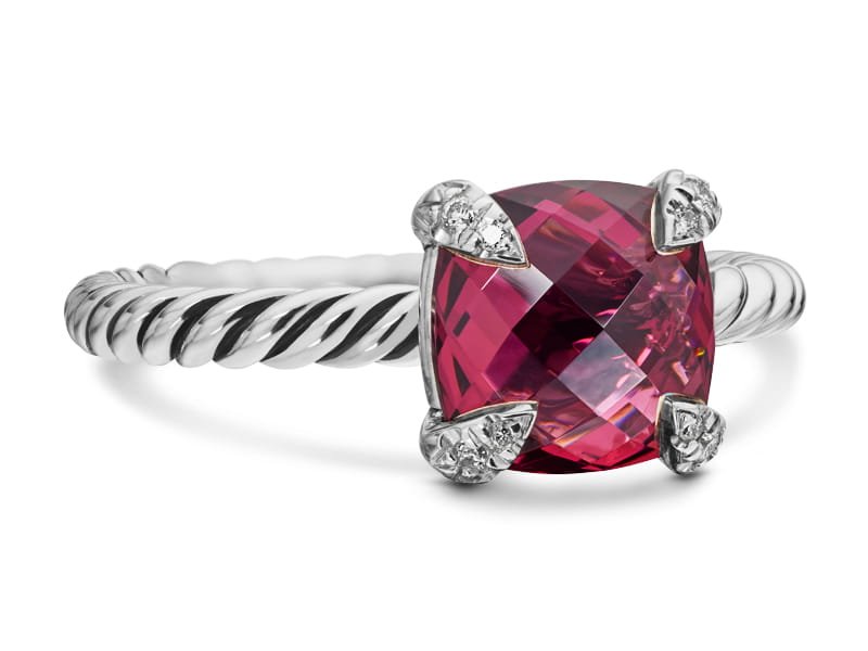 Silver ring with a twisted band and a cushion-cut deep pink gemstone held by four prongs with small accent diamonds.